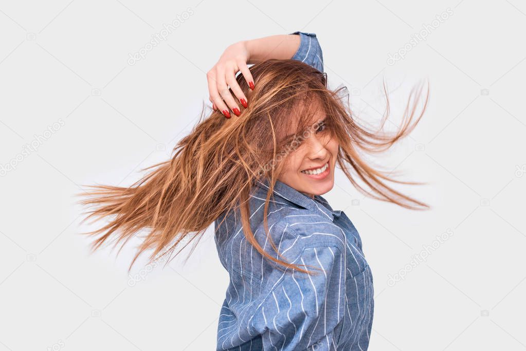 Happy cheerful woman playing with hair smilingy and laughing, posing over white background. Beautiful happy female smiles broadly with healthy white teeth and blowing hair, isolated on white wall 