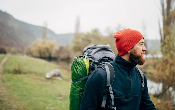 Et utendørs horisontalt portrett av en ung mann som går tur i fjell med ryggsekk og ser til en vakker utsikt. Reisende skjeggete mann som slapper av etter å ha gått. Reiser, mennesker og livsstilskonsept – stockfoto