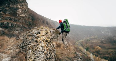 Açık havada uzun yürüyüşe çıkan kimse adam dağlarda bulutlu günde hiking dikiz. Büyük sırt çantası ve kırmızı şapka, trekking ve doğa keşfetmek seyahat erkek. Seyahat, spor, insanlar ve yaşam tarzı kavramı