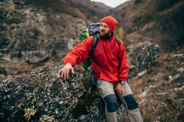 Açık havada dağ'da yürüyüş sonra rahatlatıcı kayaya oturan kırmızı giysili yorgun uzun yürüyüşe çıkan kimse adam portresi. Gezgin erkek yolculuk sırasında trekking sonra mola yok. Seyahat, insanlar, spor, yaşam biçimi