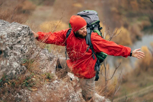 Image of young hiker man hiking in mountains dressed in red clothes exploring new places. Traveler bearded male trekking and mountaineering during his journey. Travel, people, sport, lifestyle concept — Stock Photo, Image