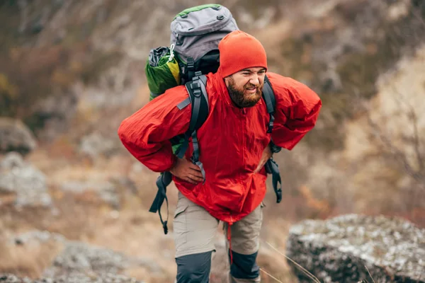 Tired hiker man hiking in mountains dressed in red clothes exploring new places. Traveler bearded male trekking and mountaineering during his journey. Travel, people, sport, lifestyle concept