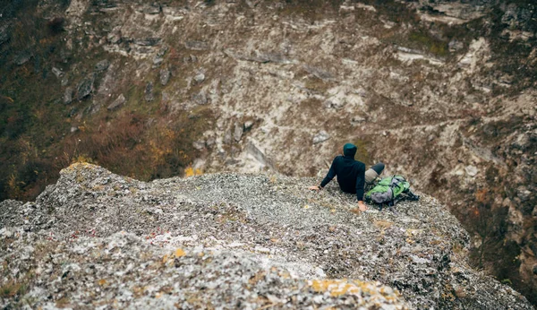 Landscape overhead rear view of hiker man relaxing in mountains after hiking. Outdoors shot of traveler male sitting alone on rock, have a break after mountaineering. Travel and lifestyle concept