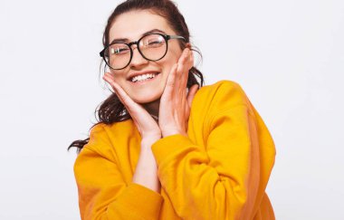 Geniş, gülümseyen güzel genç kadın portresi samimi yakından turuncu kazak ve yuvarlak şeffaf gözlük takıyor. Güzel kız öğrenci beyaz stüdyo duvardan poz. İnsanlar ve duygular