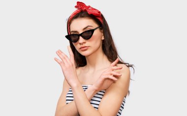 Güzel genç esmer kadın yapma dur jest elleri. Güzel kız yaz çizgili bluz, siyah şık güneş ve kırmızı kafa bandı, ret hareketi, beyaz duvara poz yapma 