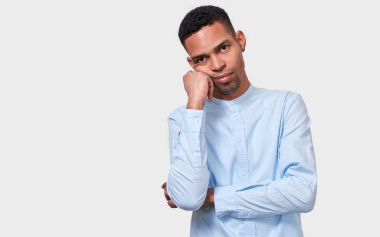 Yorgun Afro erkek yandan eğilir, ifade, rahat mavi gömlek giymiş rahatsız, beyaz stüdyo arka planı duruyor. Overworked Afrikalı-Amerikalı adam sıkılmış hisseder. İnsanlar, duygular, duygular