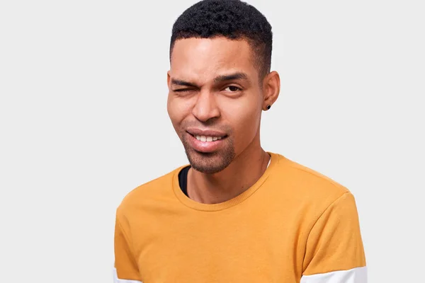 Drinnen Nahaufnahme Porträt eines gutaussehenden afrikanisch-amerikanischen jungen Mannes mit positivem Gesichtsausdruck, blinzelt mit den Augen und lächelt glücklich. Menschen, Lebensstil, Mimik und Emotionen — Stockfoto