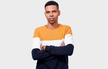 Trendy kazak giyen ciddi Afro-Amerikan yakışıklı genç çapraz eller, kamerayı beyaz stüdyo arka plan üzerinde seyir tutar. Düşünceli erkek öğrenci mezuniyet hakkında düşünme. İnsanlar