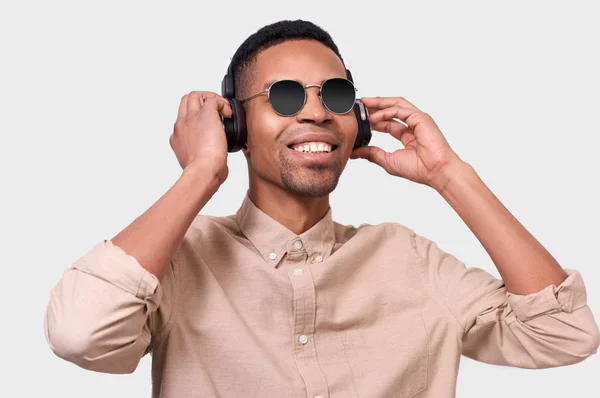 ヘッドフォン聞く音楽と踊りでアフリカ系アメリカ人の若い男の肖像画。幸せ満面の黒人男性の身に着けているミラー サングラスとカジュアルな服、白いスタジオ背景にポーズ. — ストック写真