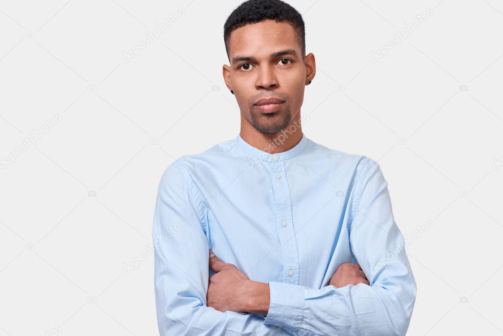 Image of serious African American young man stands with arms crossed, isolated on white background, looks on the camera, listens someone. People, ethnicity, emotions and facial expressions