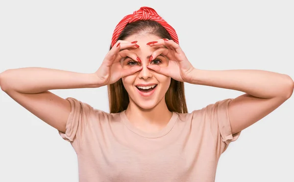 Nahaufnahme Porträt einer glücklichen jungen Frau mit rotem Stirnband, die mit beiden Händen in Ordnung gestikuliert und vorgibt, eine Brille ohne Fernglas zu tragen. hübsche Frau lächelt breit, posiert auf weißem Hintergrund. — Stockfoto