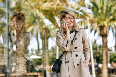 Akıllı telefonda arkadaşıyla konuşurken geniş bir şekilde gülümseyen genç güzel kadının açık hava görüntüsü, güneşli bir günde şehirde açık havada gezinme. Mutlu kadın cep telefonu konuşuyor, iyi haber var.