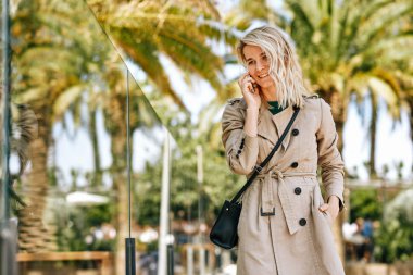 Genç ve güzel bir kadın akıllı telefonda arkadaşlarıyla konuşurken geniş bir şekilde gülümsüyor güneşli bir günde açık havada geziniyor. Cep telefonuyla konuşan zarif, mutlu bir bayan, iyi haberlerim var. Kentsel yaşam tarzı