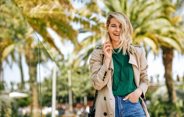 Портрет счастливой красивой блондинки, широко улыбающейся во время путешествия. Красивая женщина ходит по улице города и расслабляется в солнечный день, на фоне пальм с копировальным пространством . — стоковое фото