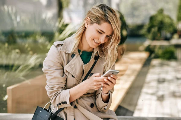 Candid ao ar livre imagem de jovem bela mulher escrevendo mensagens no smartphone, sentado ao ar livre na cidade no dia ensolarado. Mulher bonita usando wireless grátis no celular. Conceito de viagem e tecnologia — Fotografia de Stock