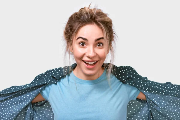 Szczęśliwy zaskoczony Młoda piękna kobieta w niebieskim t-shirt, uśmiechając się szeroko, patrząc wesoły i podekscytowany kamerą, stwarzając na białym tle Studio. Prawdziwe ludzkie emocje. — Zdjęcie stockowe