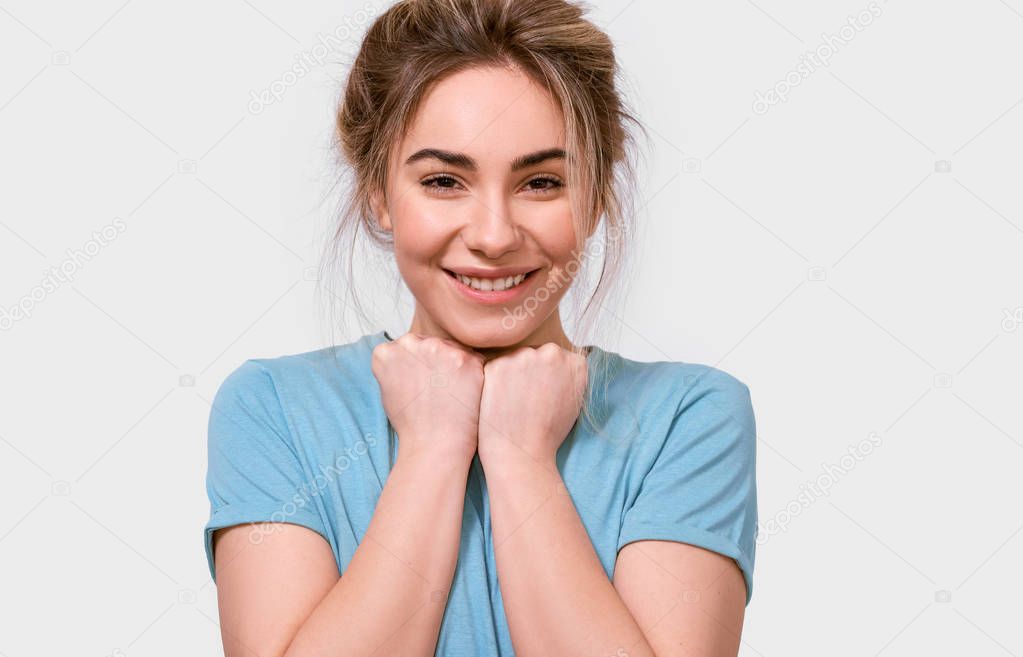 Adorable pleased young woman smiling and keeps hands on chest, looking to the camera, dressed in blue t-shirt, isolated over white background. People, emotions, feeling and body language concept