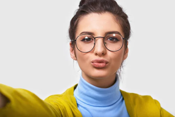 Close-up studio portret van vrolijke mooie jonge brunette vrouw met mooie schone huid, draagt transparante brillen, maken selfie over witte achtergrond. — Stockfoto