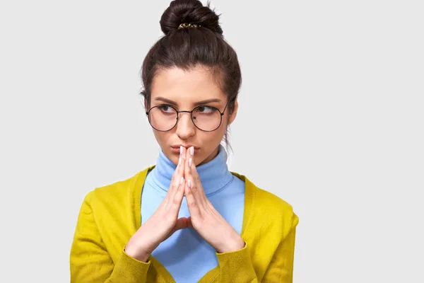 Elegante femminile, compone il piano, tiene insieme le palme, guardando da parte, indossa maglione giallo e camicetta blu, occhiali rotondi, posa su sfondo grigio, ha un aspetto intrigante. Concetto di linguaggio corporeo — Foto Stock