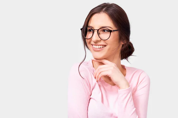 Portret całkiem pozytywnej Europejskiej młodej kobiety w różowej bluzka z długim rękawem i okrągłe przezroczyste okulary, uśmiechając się szeroko i patrząc na bok, izolowane na białym tle. Ludzie prawdziwe emocje — Zdjęcie stockowe