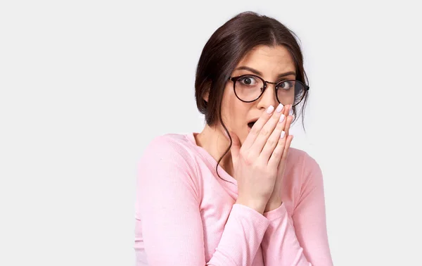 Hermosa mujer joven conmocionada lleva una blusa rosa de manga larga, mirando a la cámara, con la mano en la boca, posando sobre el fondo blanco del estudio. Primer plano retrato de la mujer sorprendida se siente sorprendido . —  Fotos de Stock