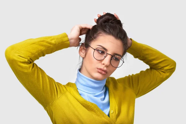 Tiro de mulher jovem bonito com pele limpa saudável, vestindo suéter amarelo e azul, fazendo um penteado nó, com expressão séria. Mulher caucasiana com cabelo reunido em grupo posando dentro de casa . — Fotografia de Stock