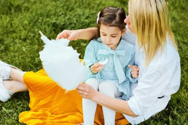 Yeşil çimenler üzerinde oturan parkta genç annesi ile pamuk şeker yiyen güzel kızı yukarıdan görünümü. Güzel kadın çocuğuna açık havada sarılıyor, birlikte vakit geçirdik. Anneler günü.