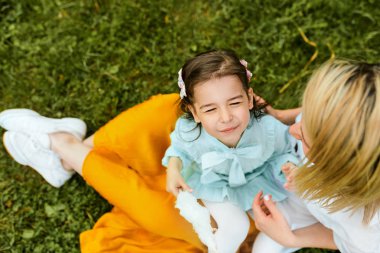 Mutlu çocuğun annesiyle birlikte dışarıda vakit geçirmenin keyfini çıkarın. Neşeli küçük kız annesiyle pamuk şeker yiyor, parkta yeşil çimenlerin üzerinde oturuyor. Anneler günü.