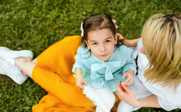 Widok z góry szczęśliwy dzieciak bawiący się z matką, ciesząc się razem na zewnątrz. Wesoła dziewczynka jedzenia Wata Cukrowa z mamą, siedząc na zielonej trawie w parku. Dzień matki. — Zdjęcie stockowe