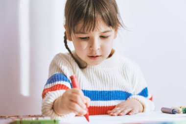 Renkli kalemler ile yaratıcı küçük kız boyama, evde beyaz masada oturuyor. Kalemlerle neşeli çocuk çizimi. İnsanlar, çocukluk ve eğitim kavramı