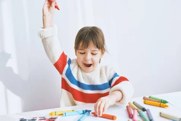 Feliz niña sonriendo y jugando con lápices de colores. Dibujo infantil alegre con lápices de colores sobre papel en el escritorio, sintiéndose feliz, sentado en casa. Personas, infancia, educación — Foto de Stock