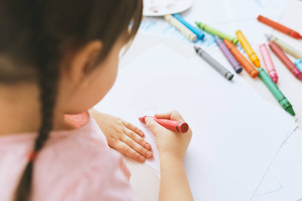 Вид сзади изображения милой маленькой девочки с красочными карандашами, носящей розовую футболку. Довольно дошкольная детская живопись и обучение в детском саду. Человек, детство, образование
