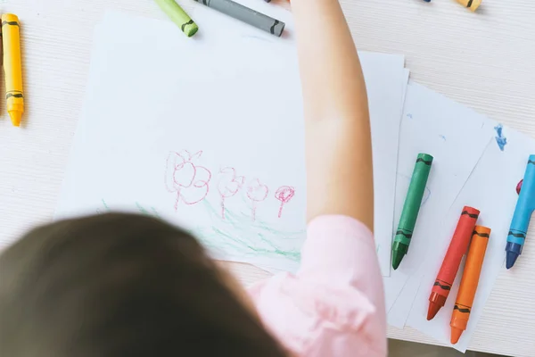Vista superior de la imagen de manos de niña dibujando con lápices de colores, vestida con camiseta rosa. Niño bastante preescolar pintando y aprendiendo en el jardín de infantes. Personas, infancia, educación — Foto de Stock