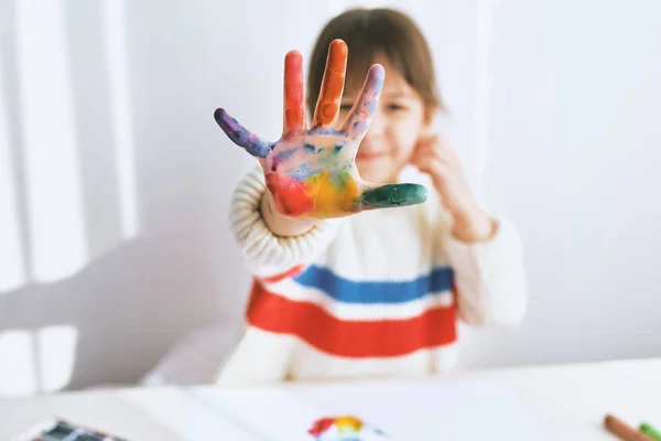 Primer plano portait de niña feliz sonriendo y mostrando su mano colorida. Pintura infantil bastante creativa y colores de aprendizaje en el jardín de infantes. Personas, infancia, educación — Foto de Stock