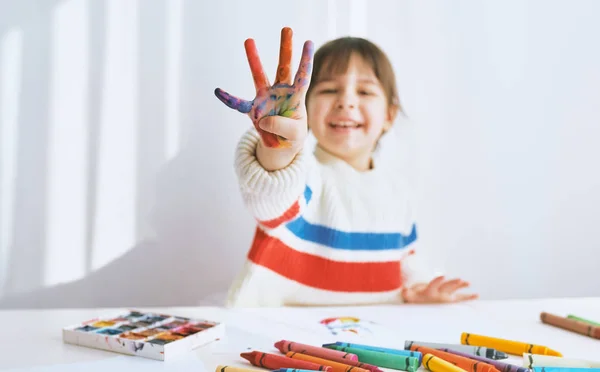 Retrato horizontal de una niña feliz sonriendo y mostrando sus dedos coloridos. Pintura infantil bastante creativa y colores de aprendizaje en el jardín de infantes. Personas, infancia, educación — Foto de Stock