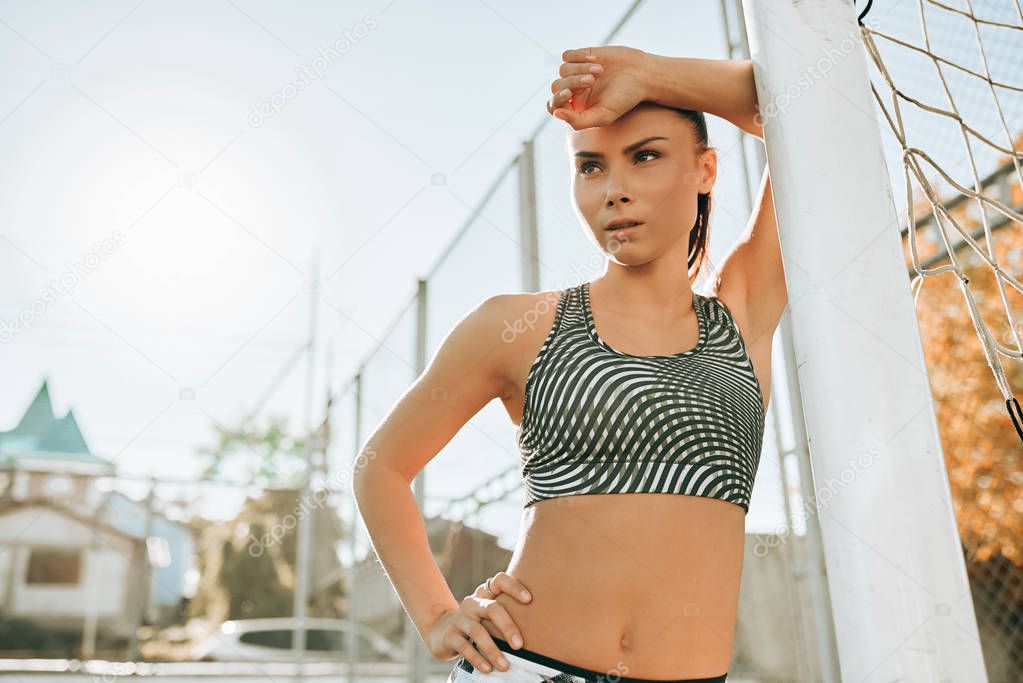 Clsoeup outdoor portrait of a young athlete woman posing and looking at the camera, resting after workout training. Sport and lifestyle concept