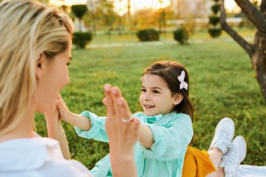 Parkta annesiyle oynayan mutlu kızın arka görüş görüntüsü. Güzel genç kadın yeşil çimenler üzerinde çocuğuile oynuyor. Anne ve küçük kız sevgiyi paylaşıyor. Mutlu çocukluk, annelik