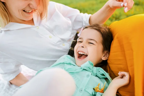 Primer plano imagen franca de niño feliz jugando con su madre, disfrutando del tiempo juntos. Linda niña riendo con mamá sentada en el césped en el parque. Madre e hija comparten el amor. Infancia — Foto de Stock