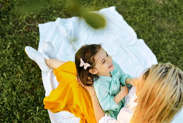 Por encima de la vista de un niño feliz mirando y sonriendo a su madre en el parque. Hermosa joven mujer y su hija pasar tiempo juntos. Mamá y la niña comparten el amor. Feliz infancia, maternidad — Foto de Stock