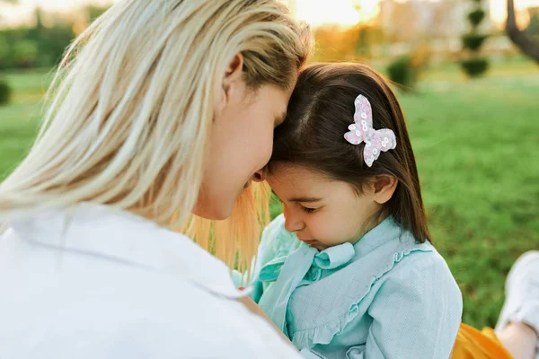 Closeup outdoor portrait of daughter hugging her mother, spending time in the park. Beautiful young woman embracing her child, sitting on the green grass. Mom and little girl shares love. Mothers day — Stock Photo, Image
