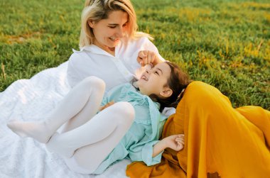 Mutlu küçük kız oynarken ve yeşil çim beyaz battaniye üzerinde annesi ile eğleniyor. Anne ve çocuk sevgiyi paylaşıyor. Anne ve kızı parkta birlikte vakit geçiriyorlar. Çocukluk ve annelik