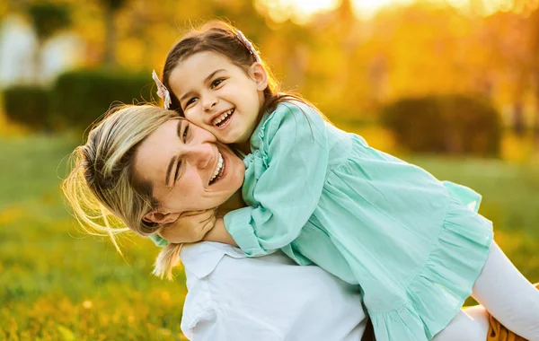 Alegre bonita hija sonriendo con su madre, pasando tiempo juntos en el parque. Hermosa joven jugando con su hijo en la hierba verde. Mamá y niña comparte el amor . — Foto de Stock