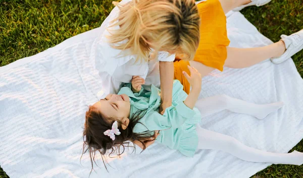 Top uitzicht van gelukkige dochter lachen met haar moeder en tijd doorbrengen samen in het Park. Jonge vrouw spelen en plezier met haar kind op het groene gras. Moeder en meisje deelt liefde. — Stockfoto