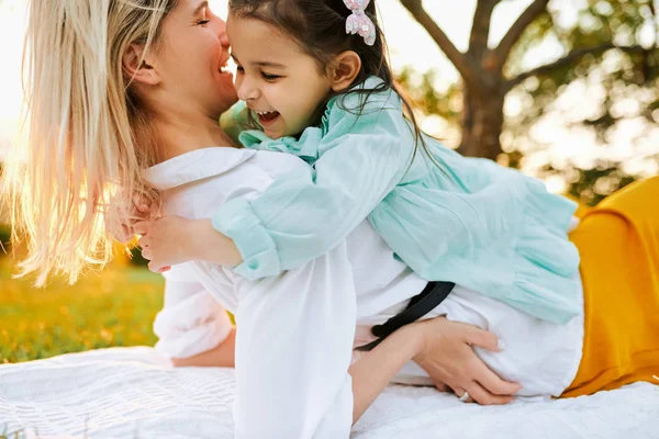 Beeld van gelukkige dochter glimlachend en knuffelen haar moeder, tijd doorbrengen samen in het Park. Jonge vrouw spelen en plezier met haar kind op het groene gras. Moeder en meisje deelt liefde. — Stockfoto