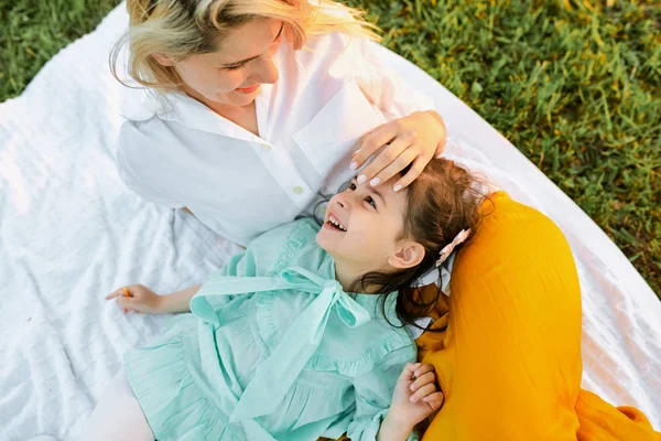 Изображение на улице счастливой девочки, играющей и веселящейся с мамой на белом одеяле на зеленой траве. Мама и ребенок разделяют любовь. Мать и дочь наслаждаются временем вместе в парке . — стоковое фото