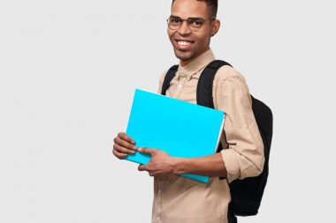 Elinde kağıtları ile mavi klasörlü rahat kıyafetli mutlu erkek öğrenci, sırt çantası gülümseyerek ve kameraya bakıyor. Genç Afrikalı Amerikalı işadamı belgeleri ile klasör tutan