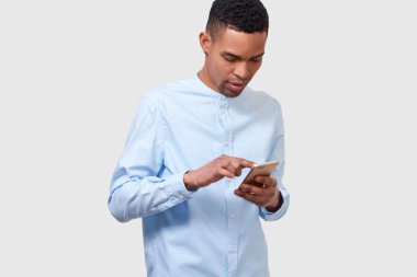 Afro-Amerikan genç adamın Stüdyo portre online haber okuma ve bloglama, modern akıllı telefon tutar. Yakışıklı Afro erkek mesajları gönderme ve internette tarama. İnsan ve teknoloji kavramı