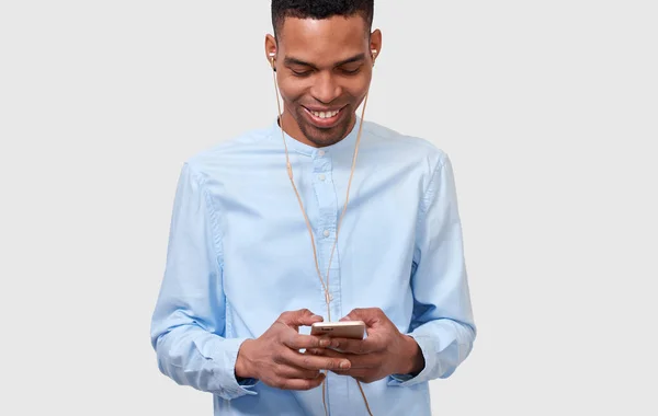 Молодой афроамериканец держит современный смартфон, читает онлайн новости и ведет блог. Красивый афро-мужчина улыбается и отправляет сообщения своему другу через интернет. Люди и технологии — стоковое фото