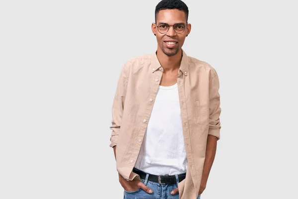 Vízszintes kép csinos mosolygó afro-amerikai fiatal férfi viselt kerek trendi szemüveg, mosolygott, és keresi a kamerát. Diák férfi pózol a fehér stúdió falra. Copyspace reklám — Stock Fotó