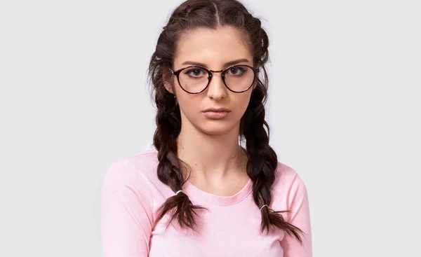 Indoor closeup portrait of overworked young brunette woman has tired facial expression, wears eyewear and pink casual blouse, isolated over white background. Shot of pretty sad female over gray wall — Stock Photo, Image